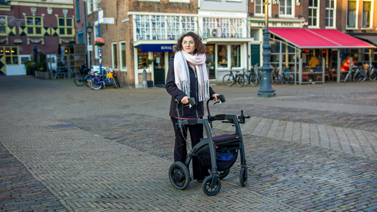 Oudere persoon loopt met een rollator over straat